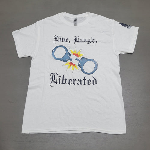 A white short-sleeve graphic t-shirt laid flat on a gray surface. The shirt features a graphic of handcuffs with a yellow and orange explosion in the center, flanked by the black gothic text 'Mine, Laugh,' and 'Liberated'.